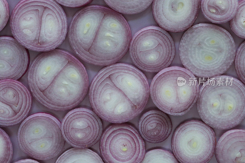 红洋葱(Allium cepa)切片的全画幅图像铺在紫色的背景上，展示白色的果肉和紫色的皮肤，健康饮食海报壁纸背景设计，高架视图